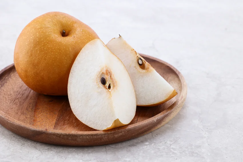 황금빛 껍질을 가진 싱싱한 배 여러 알과 수분이 가득해 보이는 하얀 배 과육 단면