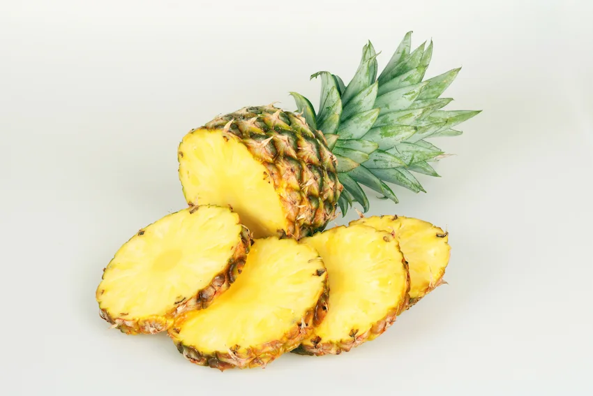 흰색 배경 위에 놓인 신선한 통파인애플 단면과 둥글게 썬 네 조각의 파인애플 슬라이스
