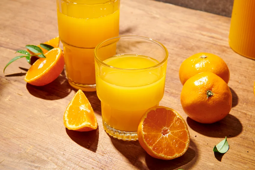 나무 테이블 위에 놓인 시원한 감귤 주스 두 잔과 반으로 잘린 감귤, 잎사귀가 붙은 신선한 귤들의 모습