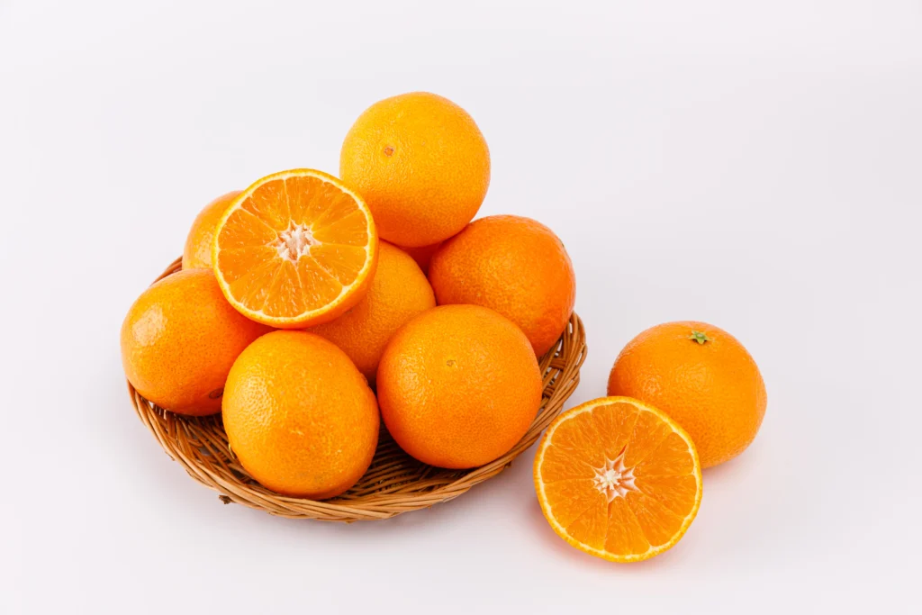 흰색 배경 위 갈색 대바구니에 담긴 신선한 레드향들과 과즙이 풍부해 보이는 반으로 잘린 레드향 단면들