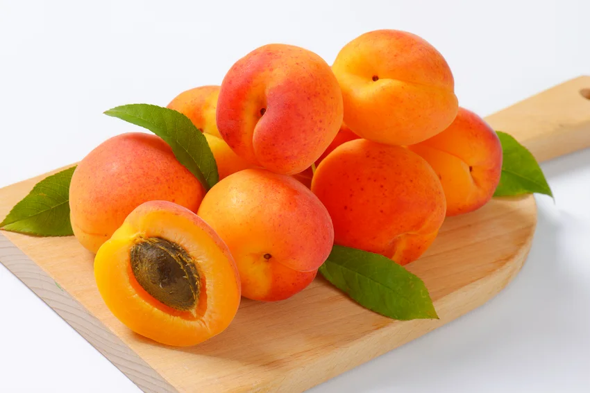 나무 도마 위에 놓인 신선한 주황색 살구들과 씨앗이 보이게 반으로 잘린 살구 단면