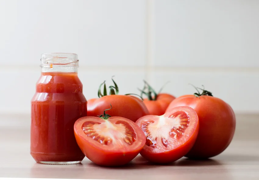 토마토 밝은 주방 배경에 잘 익은 빨간 토마토들과 단면, 그리고 유리병에 담긴 진한 토마토 주스가 놓인 모습
