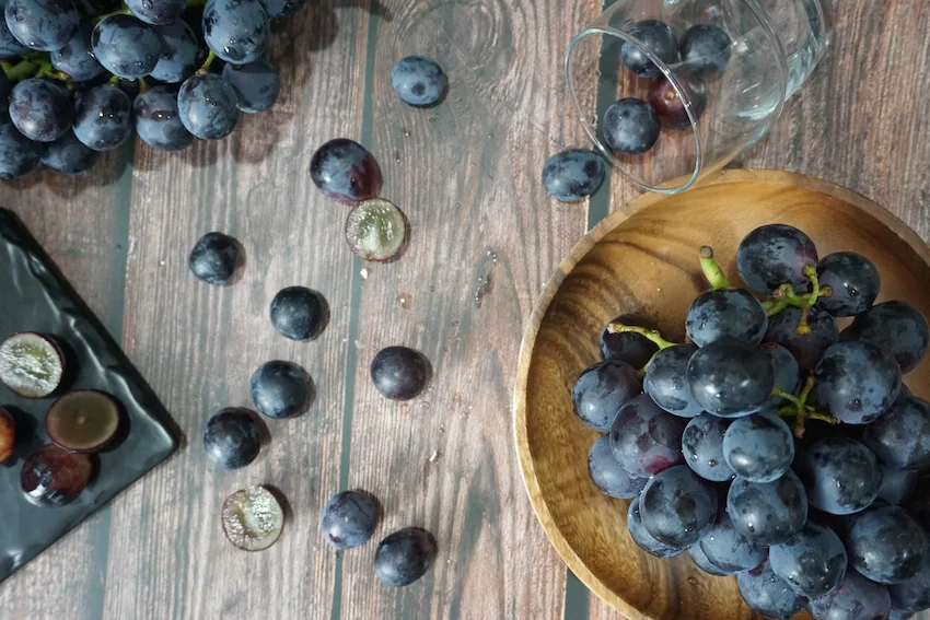 거봉, 나무 테이블 위 우드 볼에 담긴 싱싱한 거봉 포도와 주변에 흩어진 포도 알알들, 그리고 단면이 보이는 연출 사진