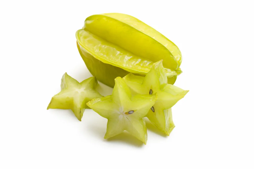 스타프루트 연두색 빛이 도는 신선한 스타프루트 한 알과 그 앞에 겹쳐진 별 모양 조각들이 놓인 사진