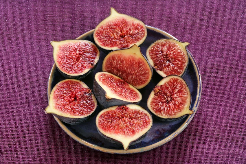 무화과, 짙은 보라색과 초록색이 섞인 잘 익은 무화과들이 나무 바구니에 자연스럽게 담겨 있는 모습